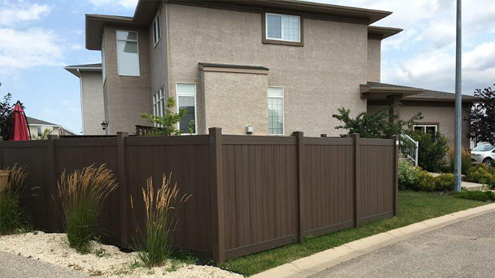 Dark brown solid privacy vinyl fencing in front of a house, an example of our Carson PVC fence panels.