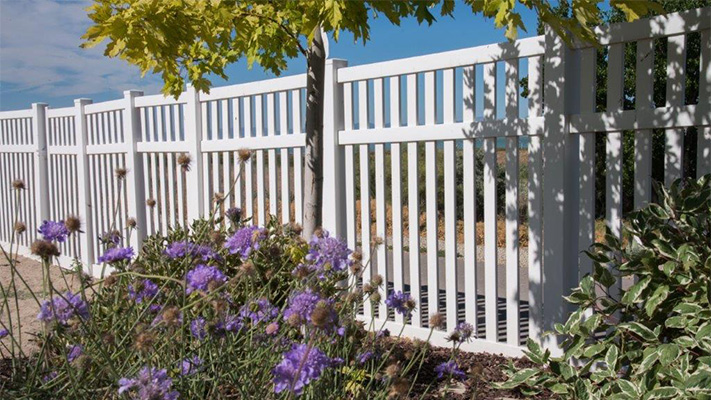 White closed picket fencing behind purple flowers, some of our best vinyl fence panels near Prather, California.