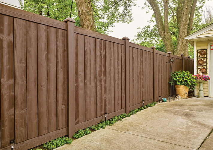 A stretch of brown Sherwood SimTek composite fence panels to the left of a home garage, an example of our Tollhouse molded plastic fencing.