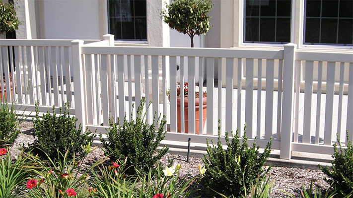White closed picket vinyl fencing next to shrubs, some of our best HOA fencing for Valencia homes.