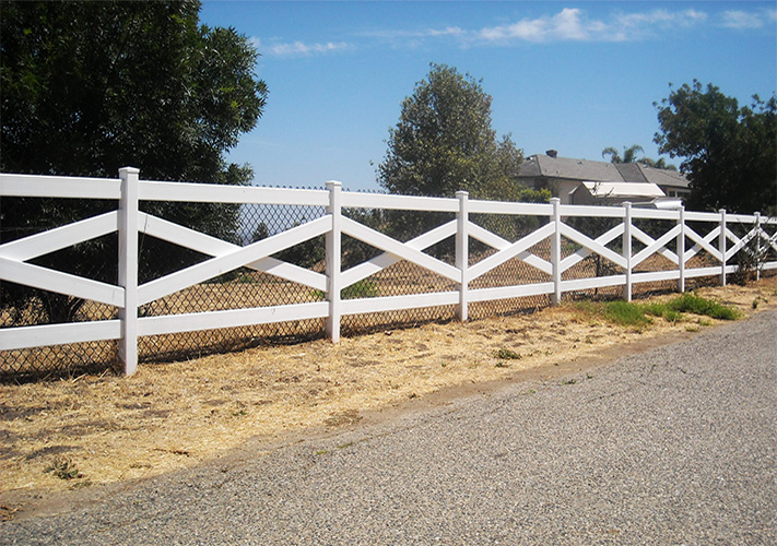 White cross buck Goshen vinyl ranch rail fencing next to a road.