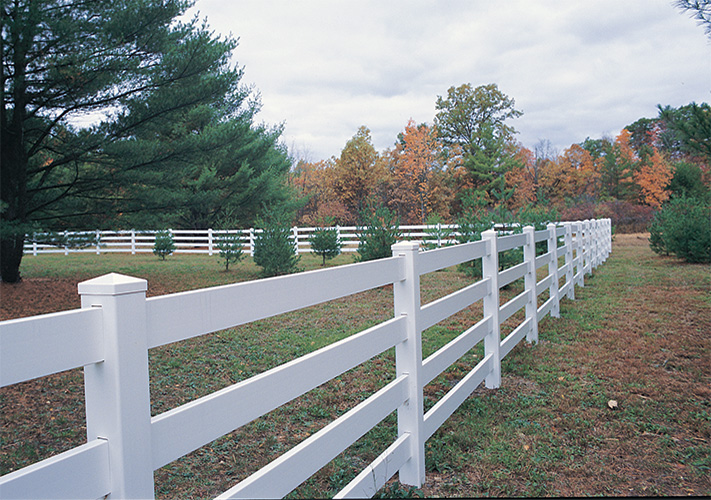 White 4-rail ranch rail fences near Northridge creating perimeter in grassy area with trees.