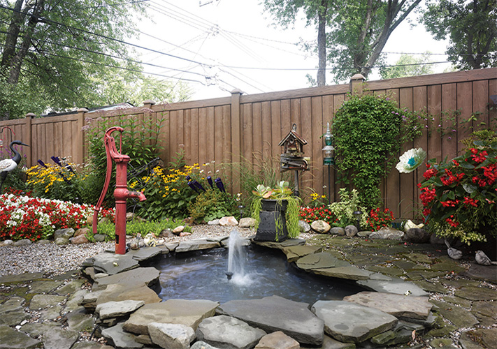 Brown faux wood fence panels near Carson, California, behind a garden and mini pond.